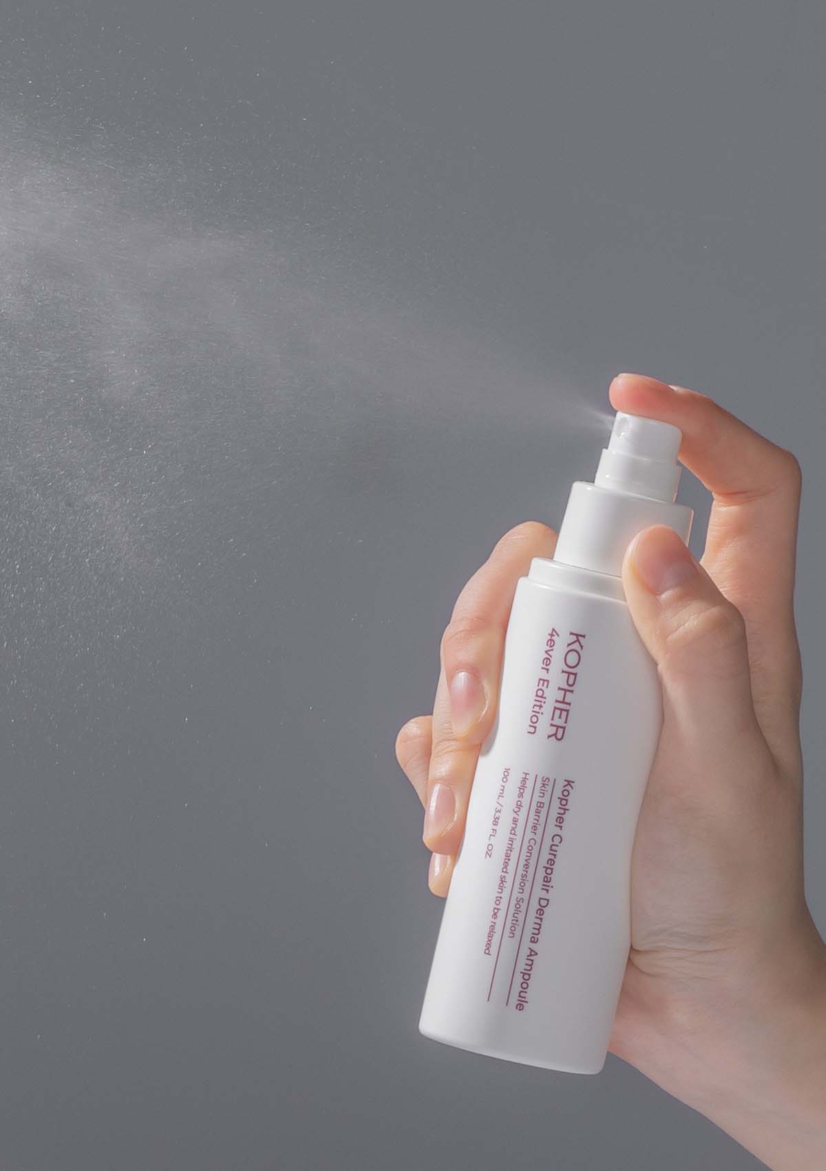 Hand holding a white spray bottle labeled 'KOPER' against a gray background